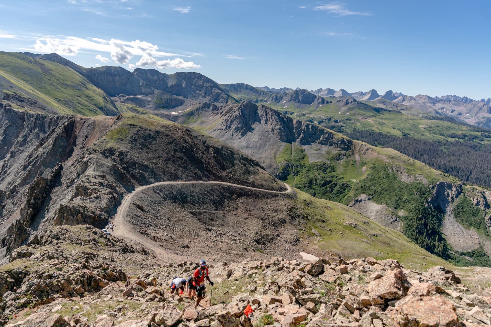 Runners climbing a switchback trail along a high alpine ridge