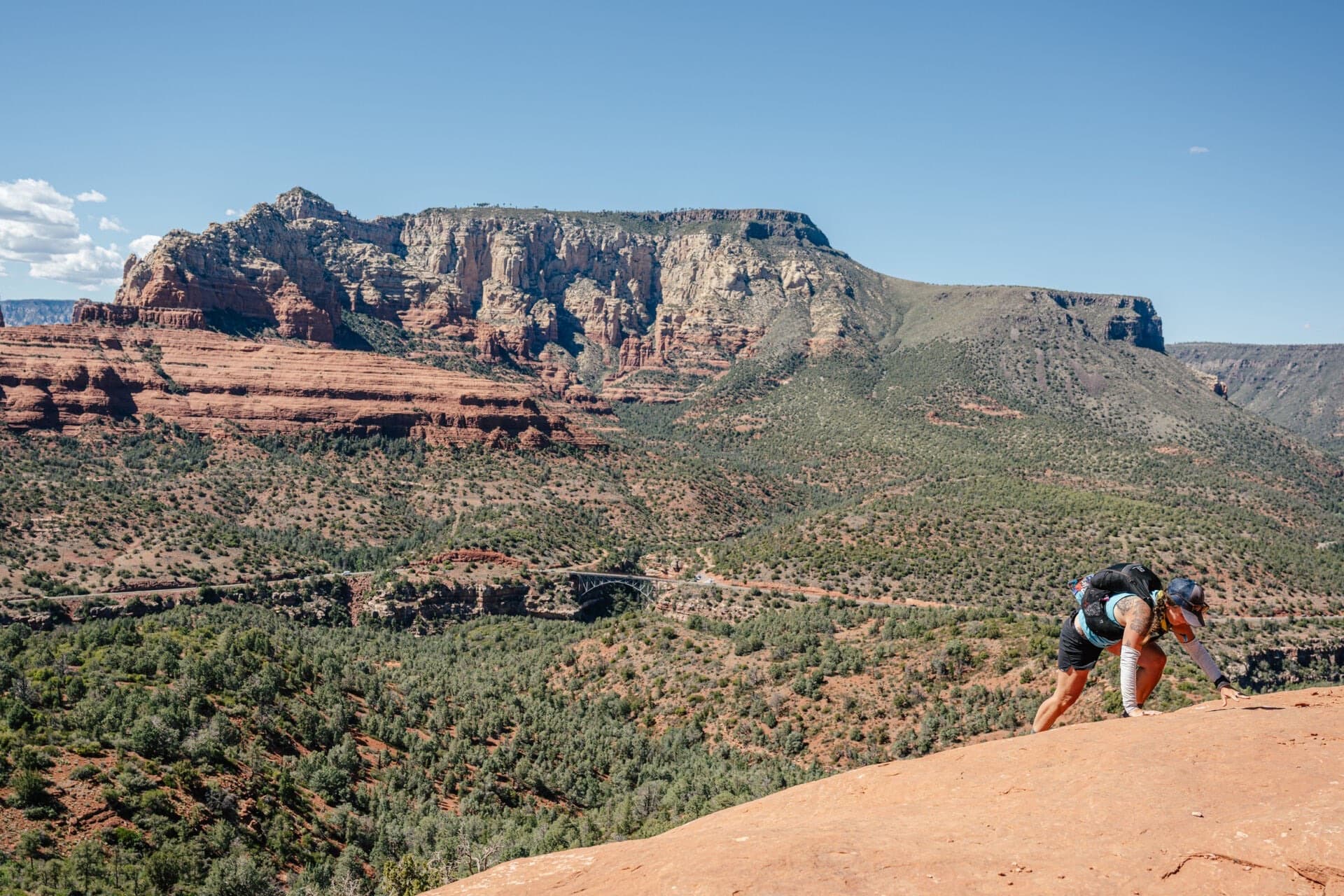 A Cocodona 250 runner scrambles up red slickrock above the Sedona valley